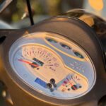 Close-up van het SYM-scooter dashboard met snelheidsmeter, brandstofmeter en km-teller in zonlicht.