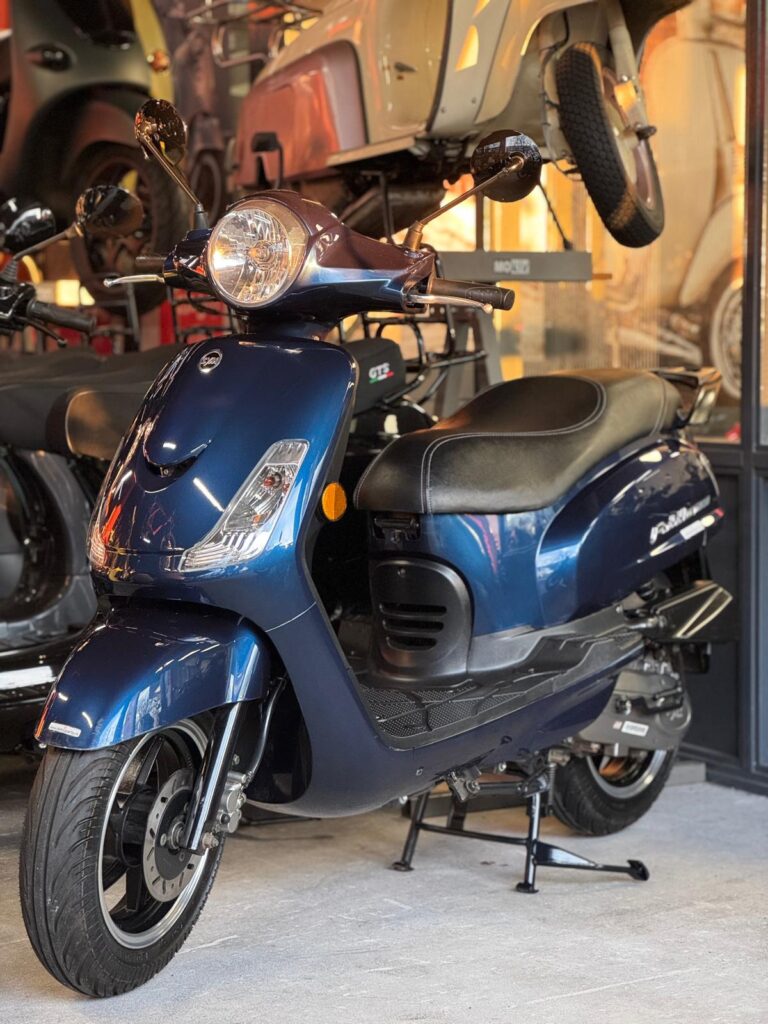 Blauwe retro-scooter op de middenbok in een showroom met andere scooters op de achtergrond.