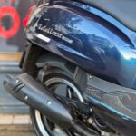 Close-up van de achterkant van een donkerblauwe scooter met uitlaat en achterwiel.