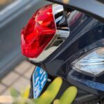 Close-up van het rode achterlicht met chroomrand en deel van kenteken van een blauwe scooter.