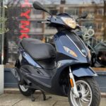 Donkerblauwe scooter op standaard, geparkeerd voor een etalage met reflecties.