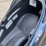 Open opbergruimte onder het zadel van een blauwe scooter, leeg en schoon.