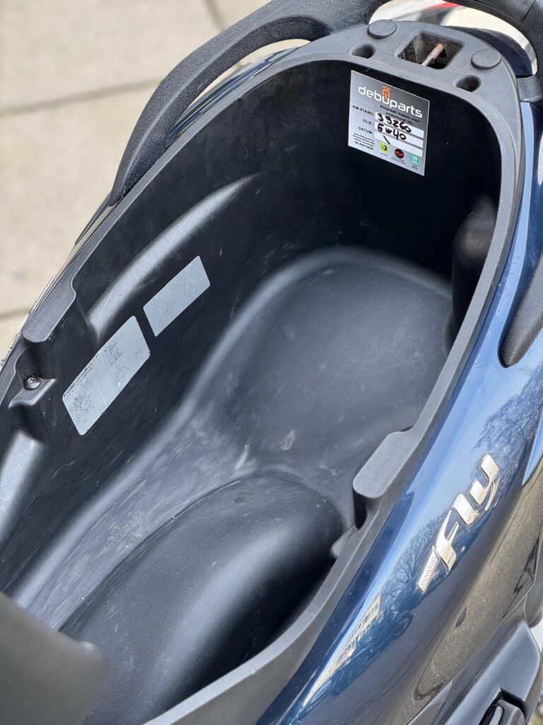 Open opbergruimte onder het zadel van een blauwe scooter, leeg en schoon.