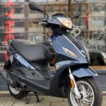 Donkerblauwe scooter op de standaard voor een winkelruit, geparkeerd op de stoep.