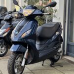 Donkerblauwe scooter met brandende koplamp op de standaard voor een winkel.