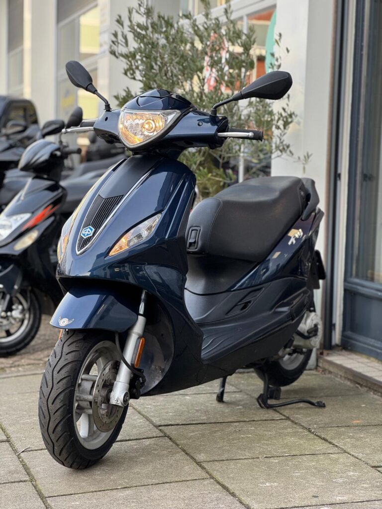 Donkerblauwe scooter met brandende koplamp op de standaard voor een winkel.