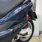 Close-up van de achterkant van een donkerblauwe scooter met zadel en rode schokdemper.