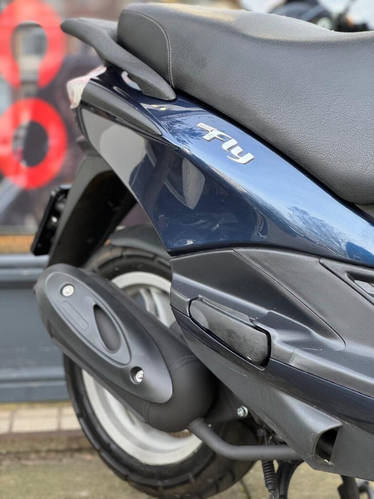 Close-up van de achterzijde van een donkerblauwe scooter met zadel, wiel en uitlaat.