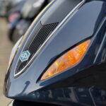 Close-up van de voorkant van een donkerblauwe scooter met oranje knipperlichten.