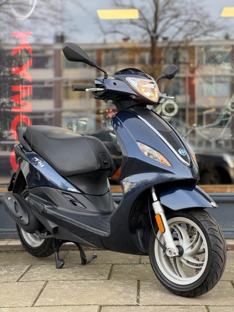 Donkerblauwe scooter op de standaard voor een winkelruit, geparkeerd op de stoep.