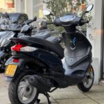 Zwarte scooter op standaard geparkeerd voor een winkel, met spiegels en gele kentekenplaat.