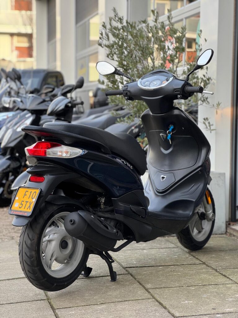 Zwarte scooter op standaard geparkeerd voor een winkel, met spiegels en gele kentekenplaat.