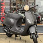 Matte zwarte scooter op de standaard voor een showroomraam, close-up van de voorkant.