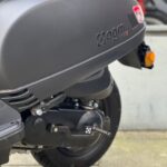 Close-up van achterzijde van een matzwarte scooter met motorblok en achterwiel.
