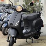 Matzwarte scooter op standaard met brandende koplamp voor een winkel, met scooters op de achtergrond.