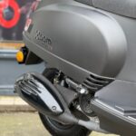 Close-up van de achterzijde met uitlaat en motorcover van een matte zwarte AGM-scooter.