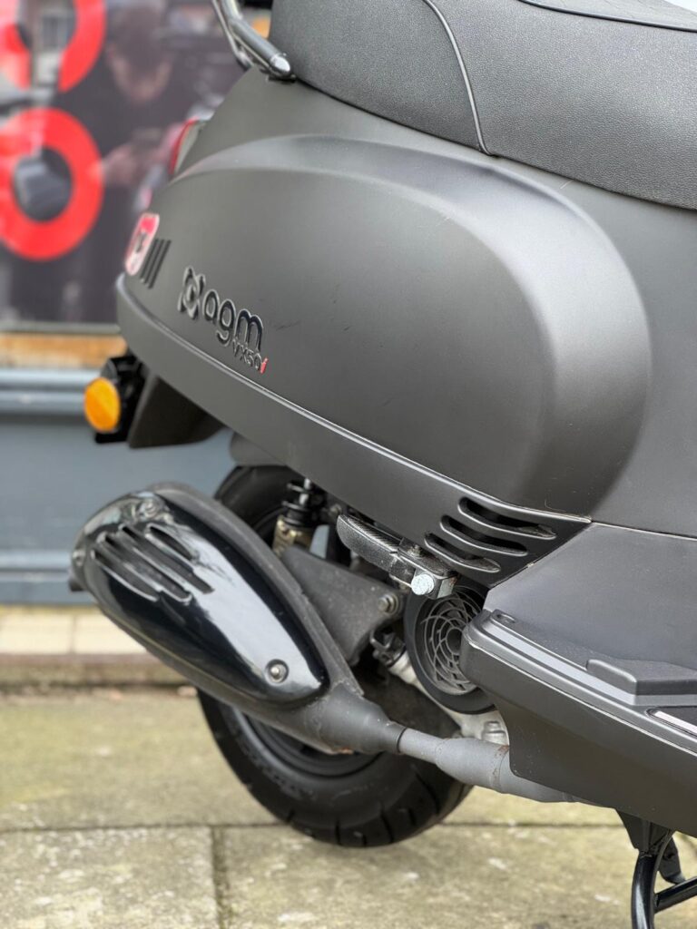 Close-up van de achterzijde met uitlaat en motorcover van een matte zwarte AGM-scooter.