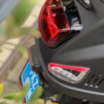 Close-up van de achterkant van een zwarte scooter met rood achterlicht, richtingaanwijzer en blauwe kentekenplaat.