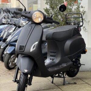 Matzwarte scooter op standaard met brandende koplamp voor een winkel, met scooters op de achtergrond.