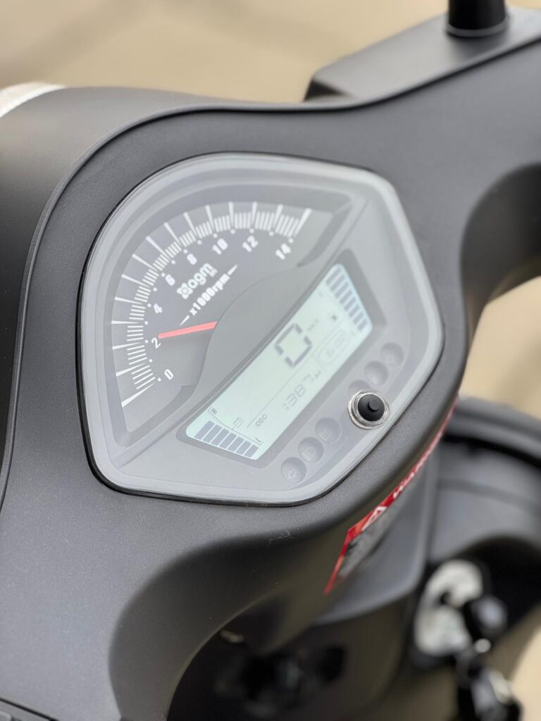 Close-up van het instrumentenpaneel van een motor of scooter met analoge toerenteller en LCD-display.