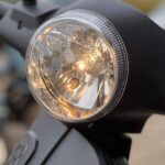 Close-up van een brandende ronde koplamp op een matte zwarte scooter.