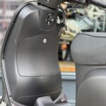 Close-up van een zwarte scooter met sleutel in het contact en zicht op stuur en voetenplank.