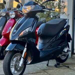 Zwarte scooter op standaard voor een winkel, met rode scooters op de achtergrond.