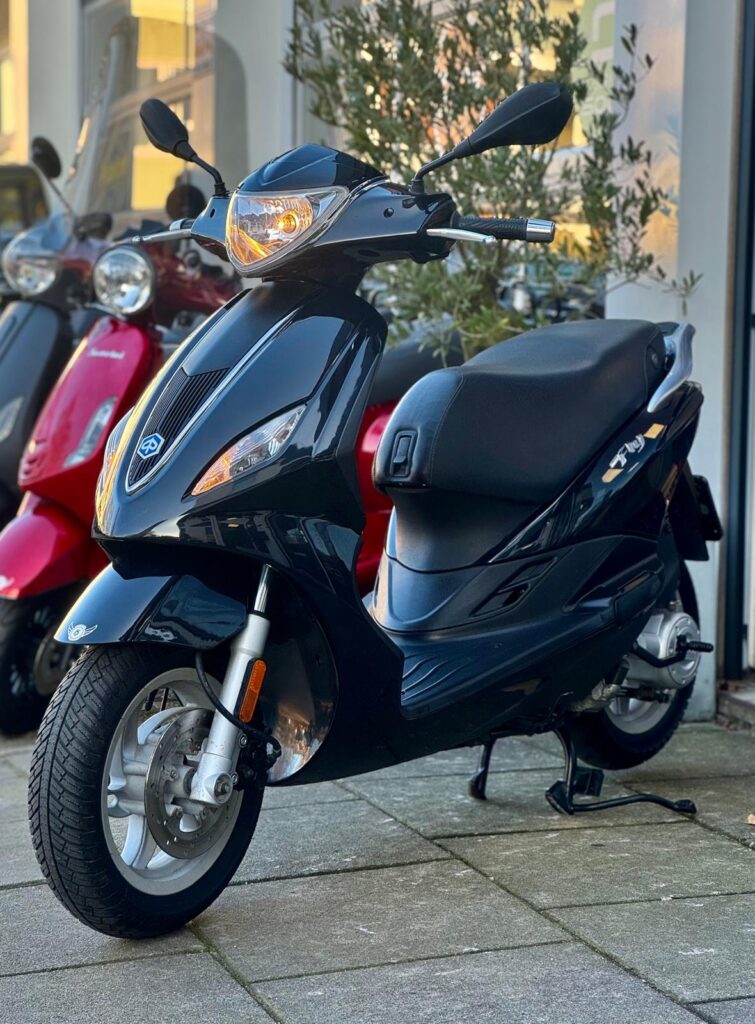Zwarte scooter op standaard voor een winkel, met rode scooter op de achtergrond.