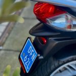 Close-up van de achterkant van een scooter met rood achterlicht en blauw kenteken.