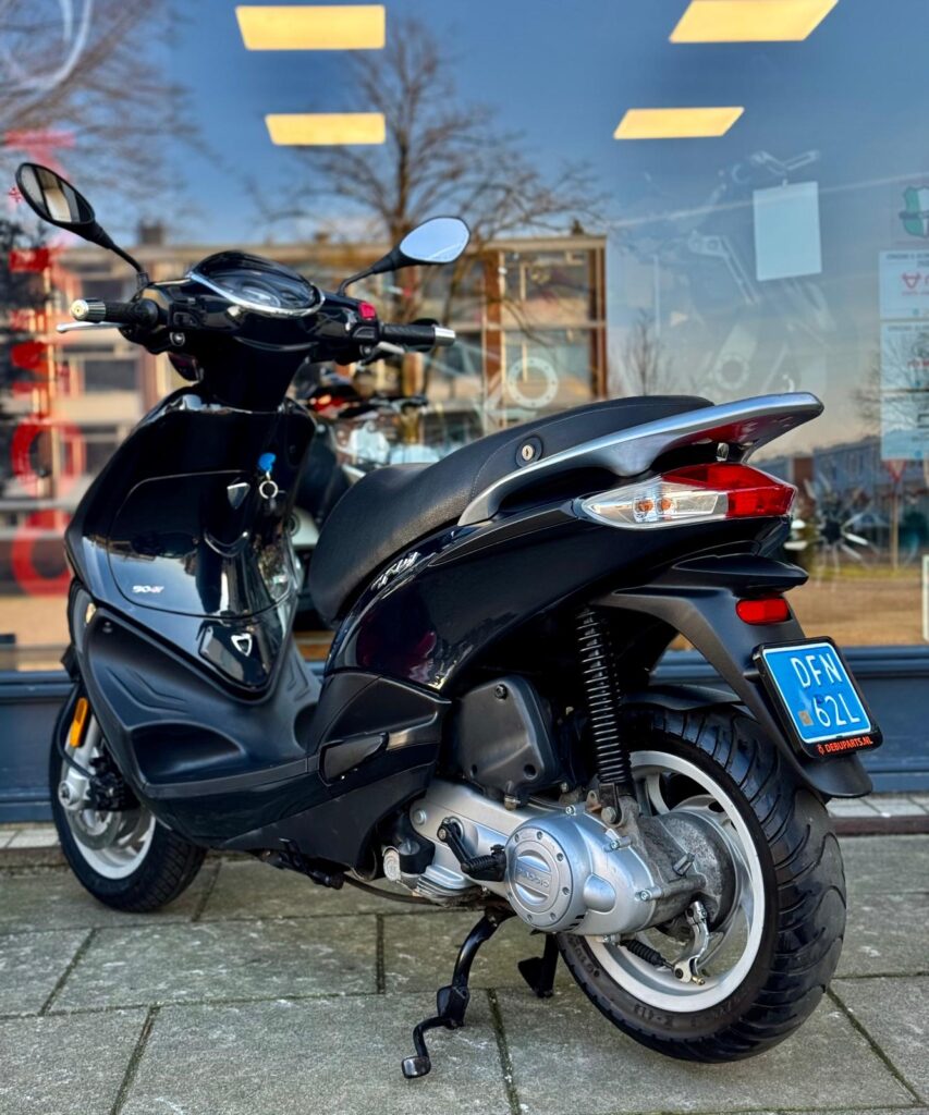 Zwarte scooter op standaard voor een winkel met glazen pui en weerspiegelingen.