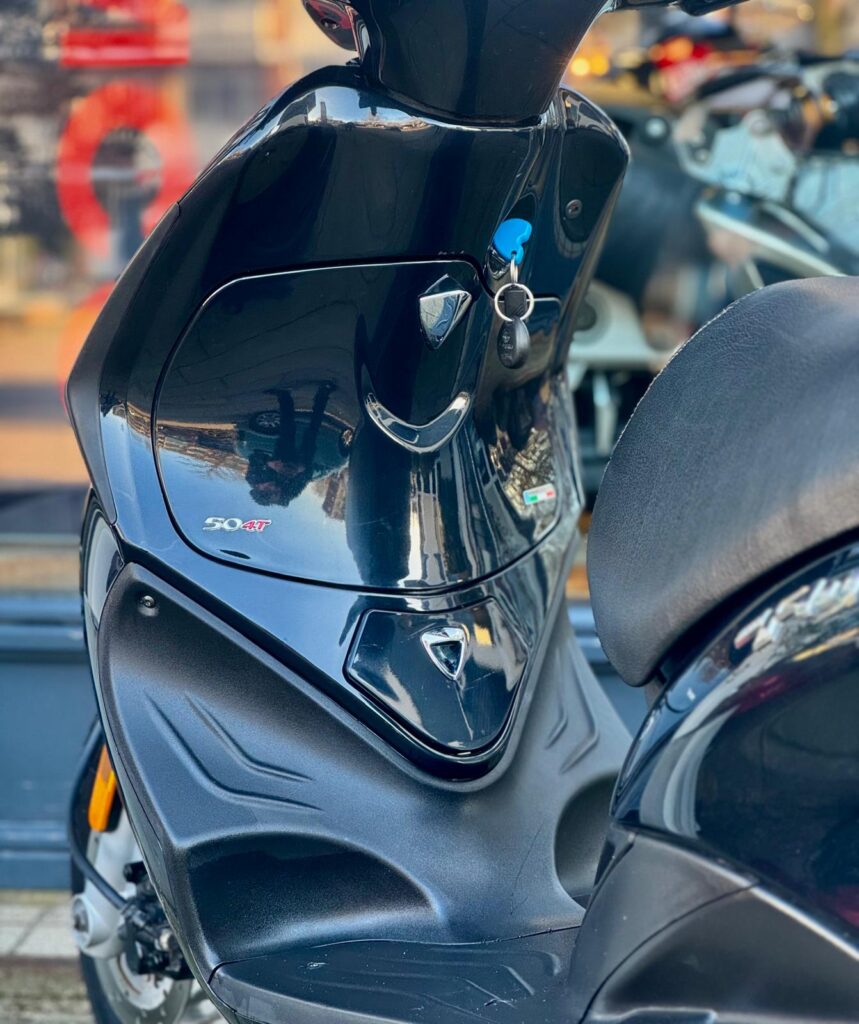 Close-up van een zwarte scooter met sleutel in het contact, 50 4T-badge zichtbaar