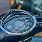 Close-up van de snelheidsmeter en het dashboard van een scooter met chroomrand, kilometerstand zichtbaar.