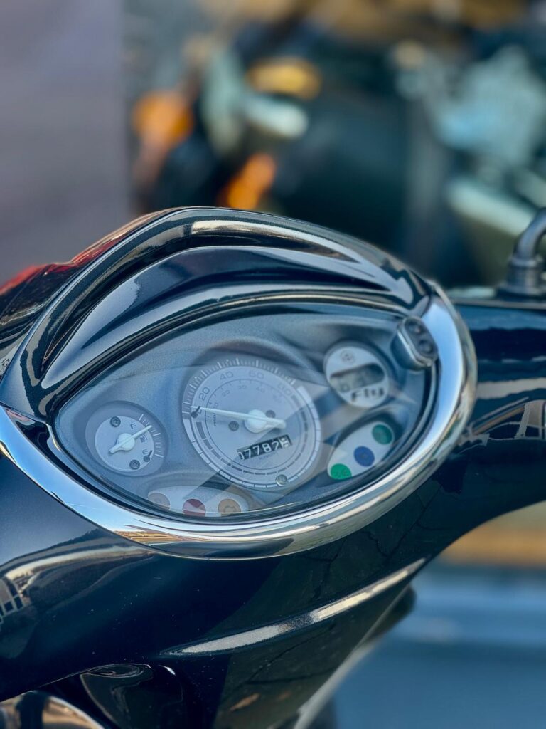 Close-up van de snelheidsmeter en het dashboard van een scooter met chroomrand, kilometerstand zichtbaar.