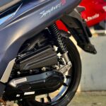 Close-up van de achterzijde van een donkerblauwe SYM Symphony ST scooter met motorblok, veer en achterwiel.