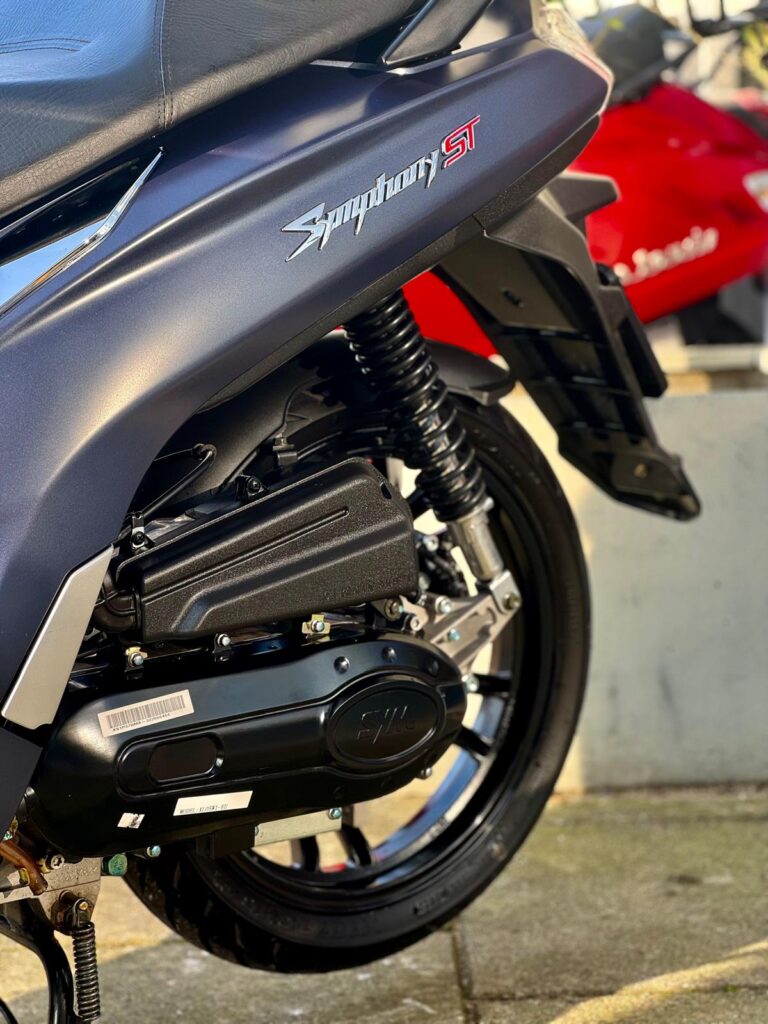 Close-up van de achterzijde van een donkerblauwe SYM Symphony ST scooter met motorblok, veer en achterwiel.