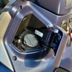 Close-up van het geopende brandstofklepje van een scooter, met dop in een klein opbergvak.