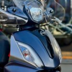 Close-up van een blauwe SYM-scooter met windscherm en koplamp, vooraanzicht.