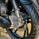 Close-up van het achterwiel van een scooter met schokdemper, remschijf en brede band.