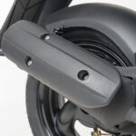 Close-up van de uitlaat en achterwiel van een scooter, mat zwarte afwerking.