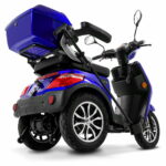 Blauwe driewielige elektrische scootmobiel met topkoffer, gezien schuin van achteren.