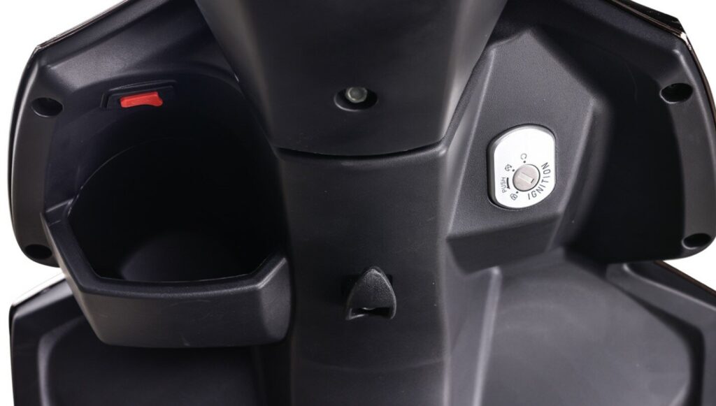 Close-up van scooter voorpaneel met contactslot, opbergvak en tashaak in zwarte kunststof.