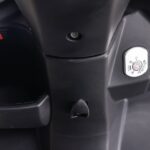 Close-up van scooter voorpaneel met contactslot, opbergvak en tashaak in zwarte kunststof.