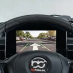 Stuur en dashboard van voertuig met achteruitrijcamera op scherm op parkeerterrein.