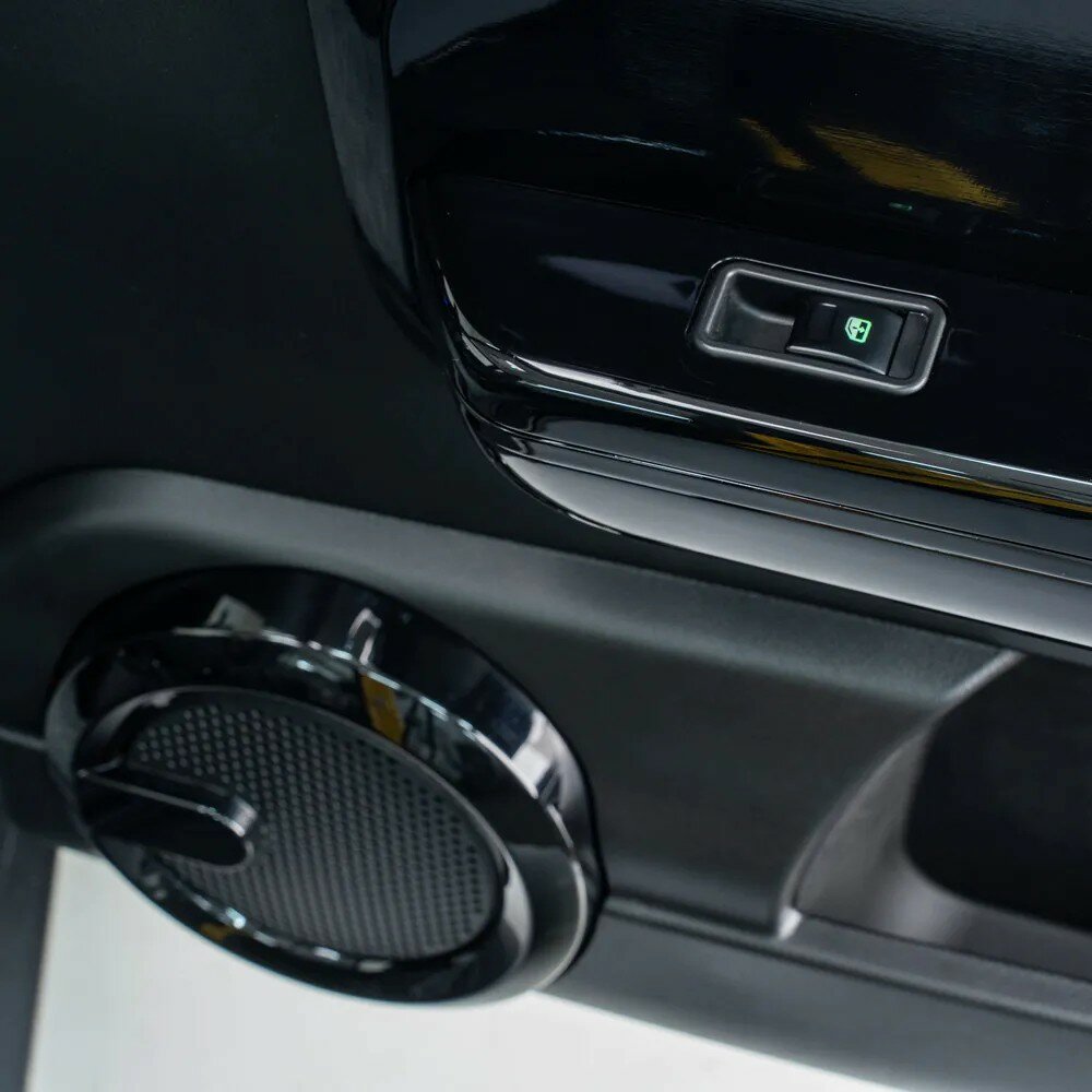 Detail van een autodeurpaneel met verlichte elektrische raamknop en ronde luidspreker.