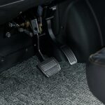 Close-up van rem- en gaspedaal van een auto op een grijze vloermat.