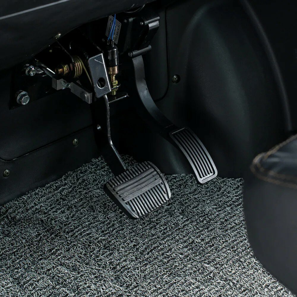 Close-up van rem- en gaspedaal van een auto op een grijze vloermat.