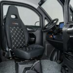 Interieur van een compacte elektrische microauto met luxe bestuurdersstoel, stuur en infotainmentscherm.