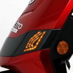 Close-up van de voorkant van een rode scooter met brandende oranje LED-knipperlicht en reflector.