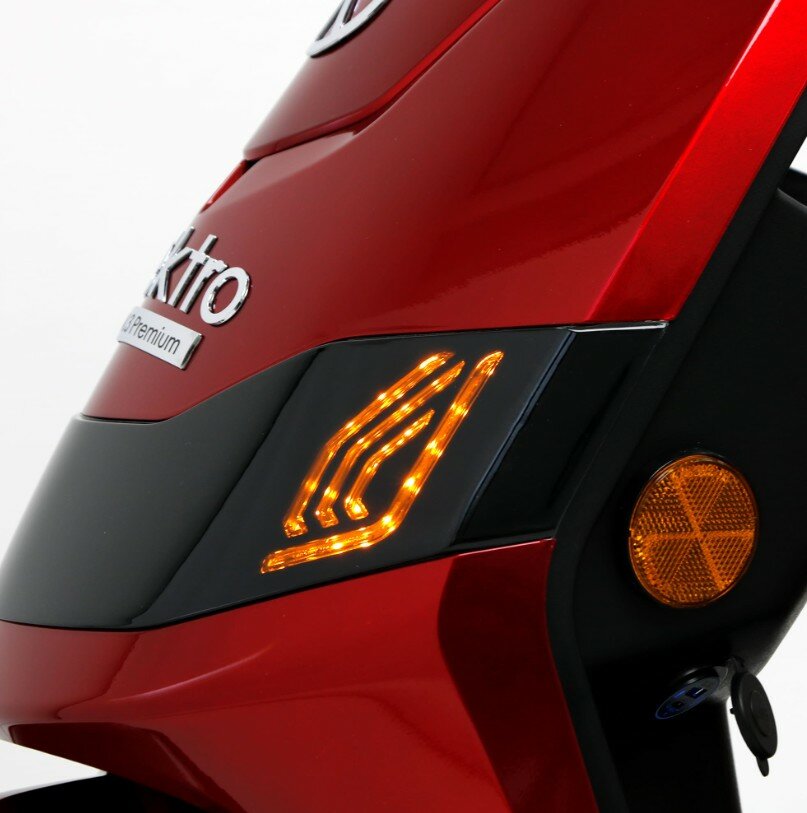 Close-up van de voorkant van een rode scooter met brandende oranje LED-knipperlicht en reflector.