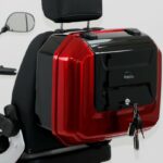 Rood-zwarte topkoffer met sleutels in het slot, gemonteerd achterop een scooterstoel.